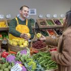 Man in yellow apron and woman exchanging fresh fruits at a vibrant market in Madrid.