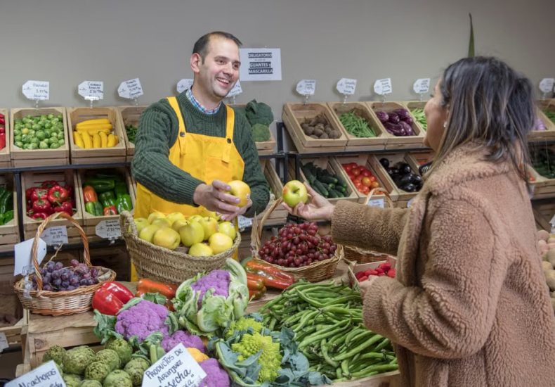 Man in yellow apron and woman exchanging fresh fruits at a vibrant market in Madrid.